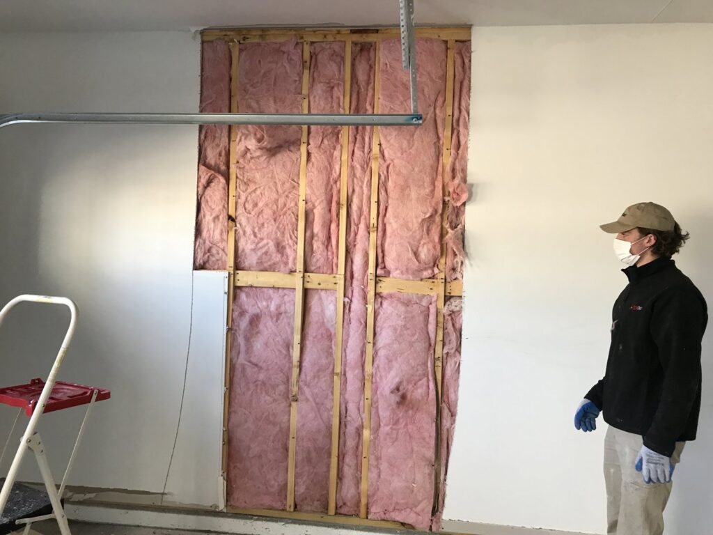 A PuroClean technician inspecting a wall with exposed insulation during water damage remediation in Northport, AL.