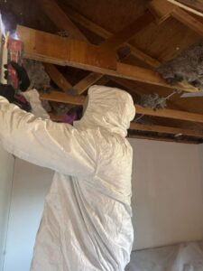 A worker in a protective suit performing water damage remediation on an exposed ceiling for Highway Renovation in Twin Falls, ID.