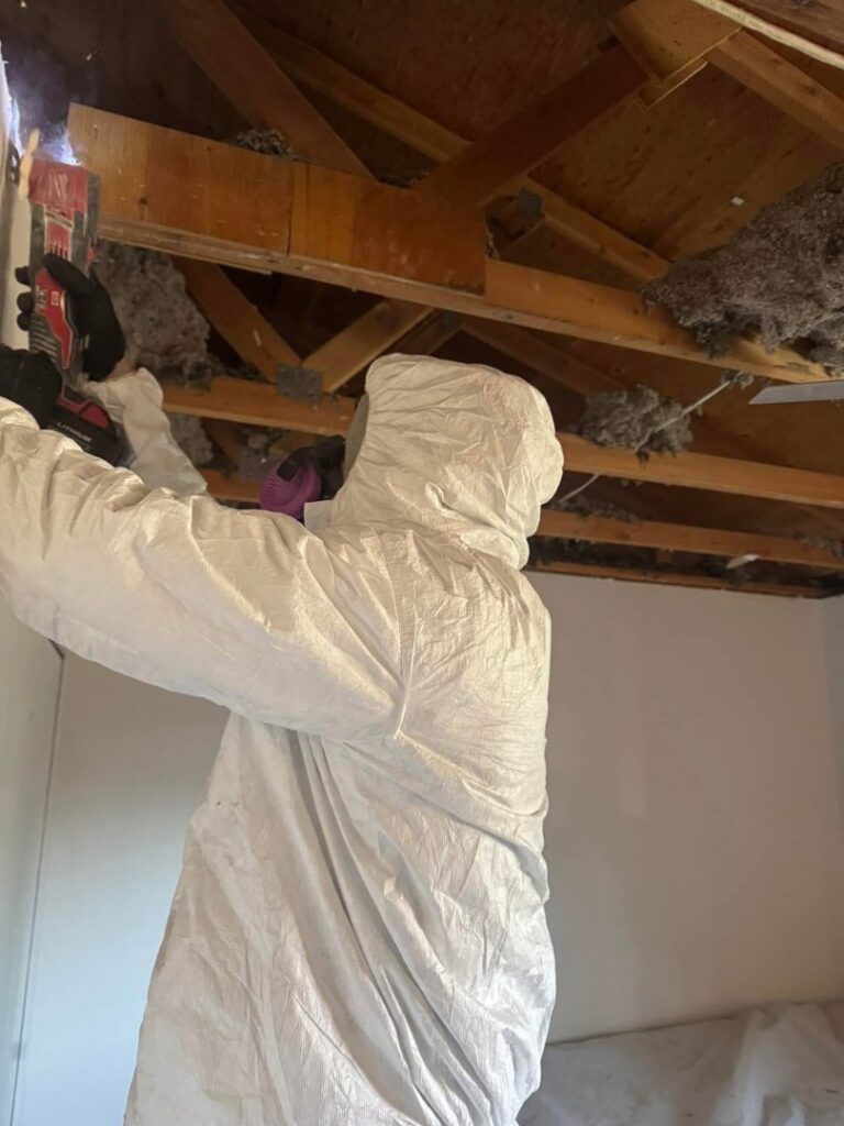 A worker in a protective suit performing water damage remediation on an exposed ceiling for Highway Renovation in Twin Falls, ID.