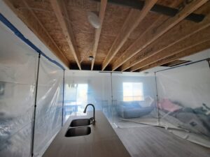 A kitchen area with plastic containment sheeting and exposed ceiling joists during water damage restoration by Flood Pros in Sandy, UT.