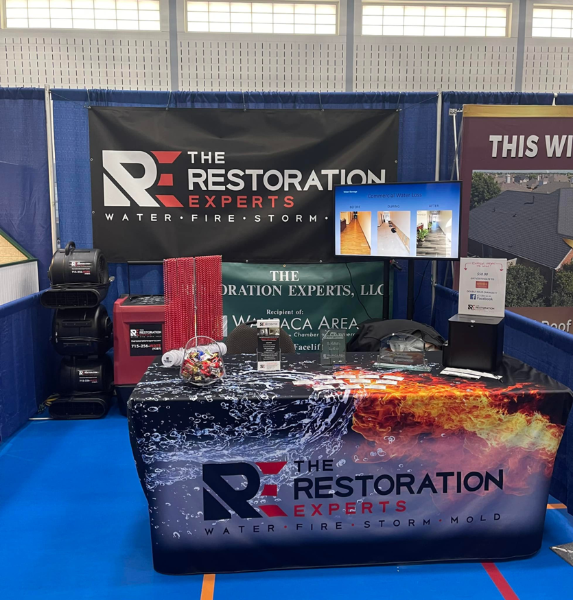 A display booth featuring water damage restoration equipment and branding for The Restoration Experts in Waupaca, WI.
