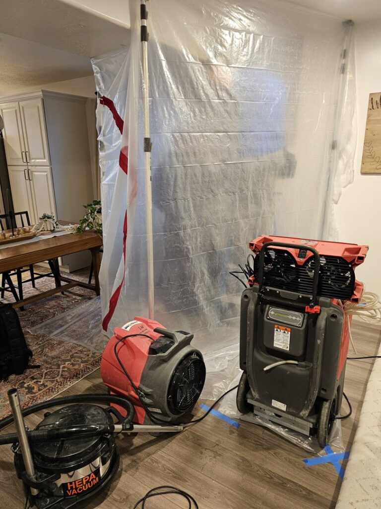 Water damage restoration equipment, including an air mover and dehumidifier, set up with a containment barrier by Utah Disaster Team in Layton, UT.