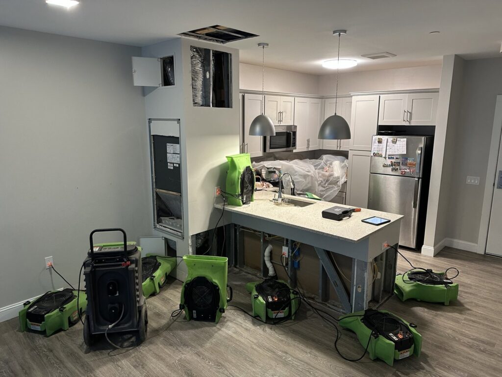 Water damage restoration equipment, including air movers and dehumidifiers, set up in a kitchen and living area by Servpro of Dartmouth / New Bedford in New Bedford, MA