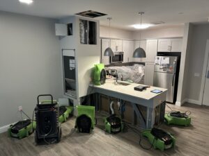 Water damage restoration equipment, including air movers and dehumidifiers, set up in a kitchen and living area by Servpro of Dartmouth / New Bedford in New Bedford, MA