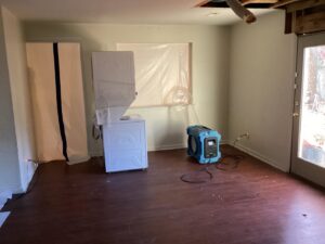 A room undergoing water damage restoration with a dehumidifier, air mover, and plastic sheeting by Doctor Fix-It in Denver, CO.