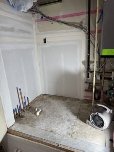 A utility room undergoing water damage restoration with an air mover and exposed pipes by Taylored Restoration in Anchorage, AK