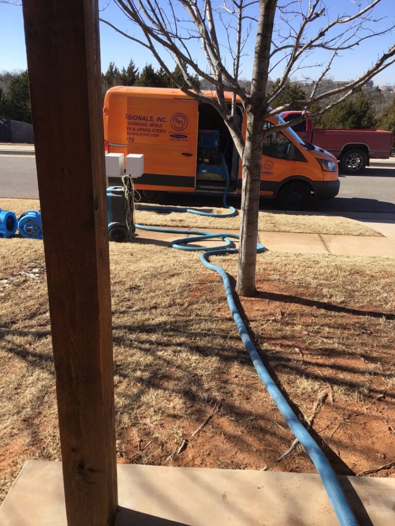 A Service Professionals van with hoses and air movers set up for water damage restoration outside a home in Edmond, OK.