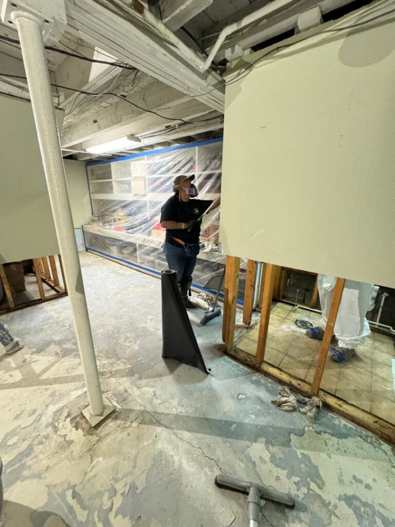 A worker preparing a basement for water damage restoration with exposed studs and protective sheeting for Island Emergency Disaster Restoration in Farmingdale, NY.