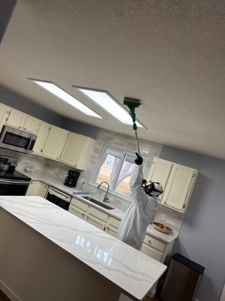 A water damage specialist from Property Doctors, Inc. in Denver, CO, cleaning a kitchen ceiling in a hazmat suit.