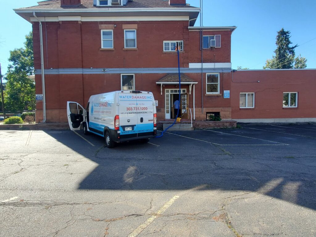 A Water Damage, Inc. specialist in a hazmat suit spraying a garage ceiling during remediation work in Denver, CO.