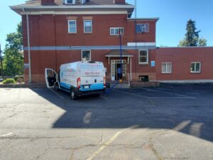 A Water Damage, Inc. specialist in a hazmat suit spraying a garage ceiling during remediation work in Denver, CO.