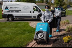 Water damage specialists from New Method Restoration in Edison, NJ, unloading a large dehumidifier from their company van at a job site.