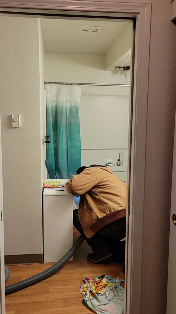 A water damage technician bending over near a bathtub, performing water extraction, for Robinson Restoration in Vancouver, WA