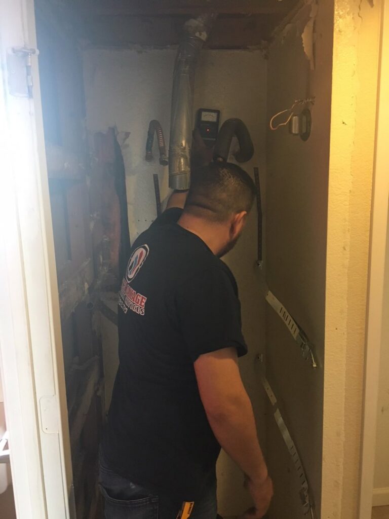 A water damage technician from EZ Water Damage Restoration Services inspecting pipes in a closet during restoration in Chula Vista, CA.