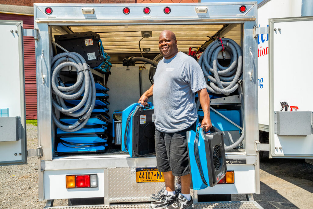 A Claim Masters water damage technician holding specialized drying equipment from a truck in New Hartford, NY.