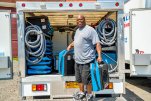 A Claim Masters water damage technician holding specialized drying equipment from a truck in New Hartford, NY.