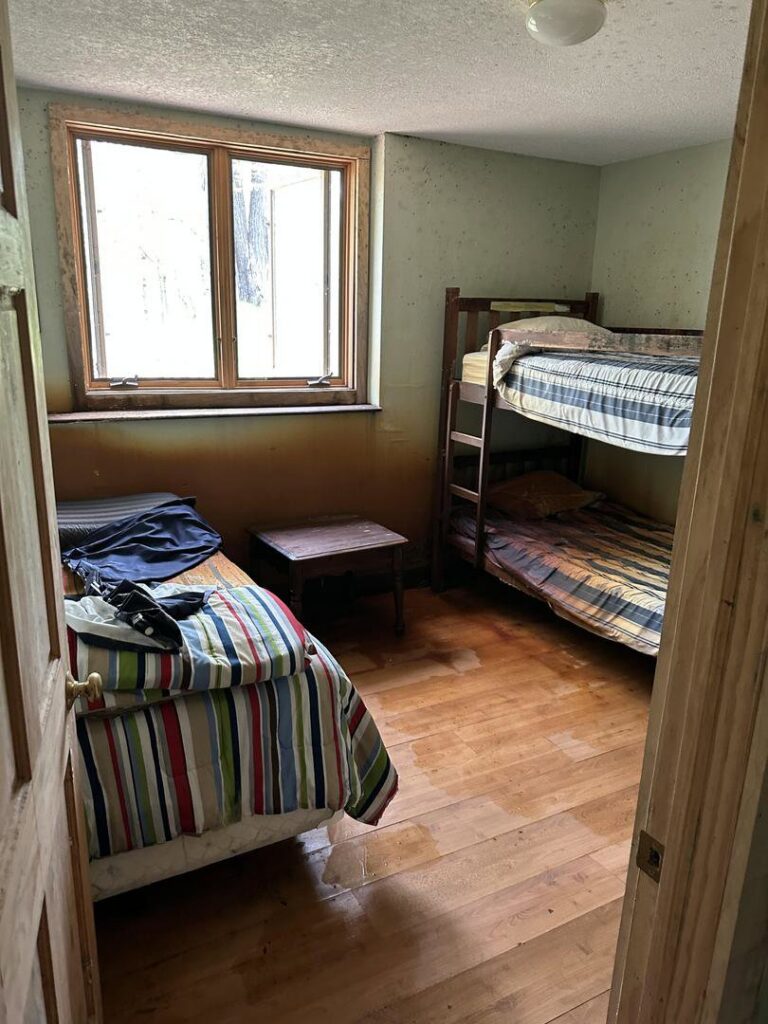 A water-damaged bedroom with wet wooden floors and stained walls, indicating a need for Restoration Alliance Services in Elk River, MN.