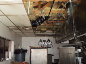 A water-damaged commercial kitchen ceiling with removed tiles and exposed pipes being restored by Servpro of Bend in Bend, OR
