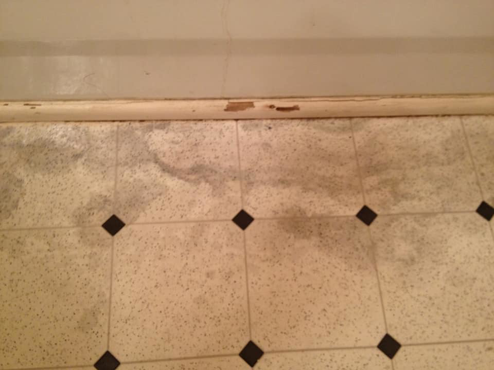 A water-damaged floor and baseboard showing stains and potential mold, addressed by Major Damage in Bentonville, AR.