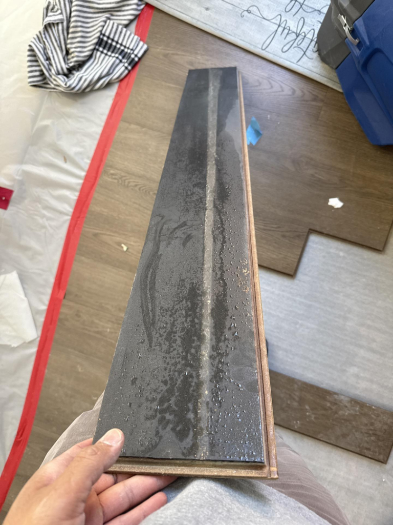 A hand holding a piece of water-damaged flooring during an inspection by Triangle Restoration in Raleigh, NC.
