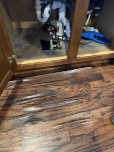 Water-damaged flooring under a sink cabinet, showing warping and discoloration, by Triangle Restoration in Raleigh, NC.
