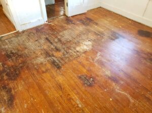 A hardwood floor showing significant dark water stains and discoloration from water damage, remediated by A1 Restoration of Spokane in Post Falls, ID.
