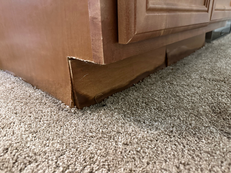 Close-up of a water-damaged kitchen cabinet base requiring restoration from USA Water Damage Thunder Restoration in Coon Rapids, MN.