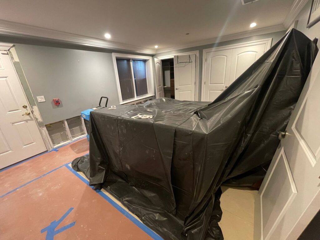 A water-damaged room with removed drywall, covered furniture, and drying equipment by NSH Home Services in Jersey City, NJ.
