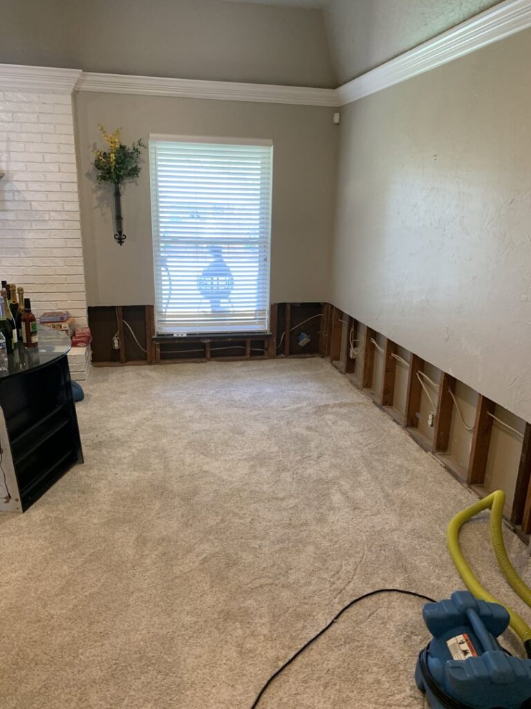 A water-damaged room with lower walls removed to expose studs for drying and remediation by Service Professionals in Edmond, OK.
