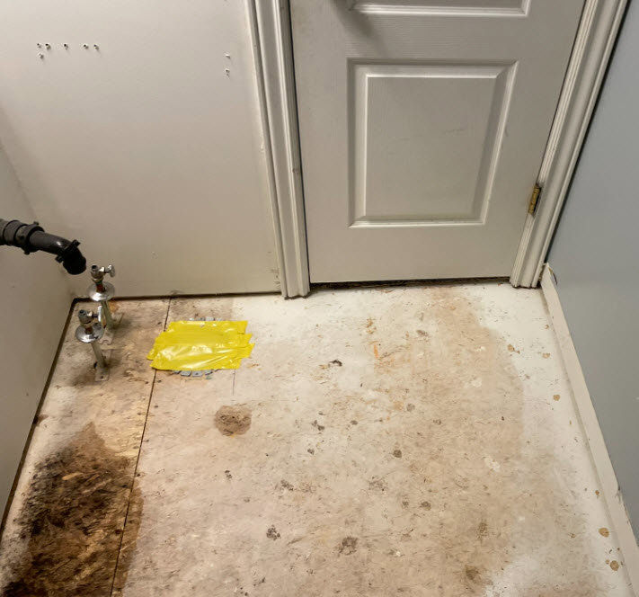 A water-damaged subfloor near a door and pipes, showing the extent of water damage restoration needed by RestoPros of Salt Lake City, UT