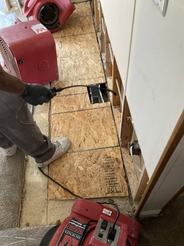 A technician removes water-damaged subfloor material with drying equipment visible at Directed Heat Restoration, Livonia, MI.