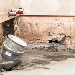 A close-up of a water-damaged wall with exposed pipes and concrete, showing demolition work by Valley Restoration in Arbuckle, CA.
