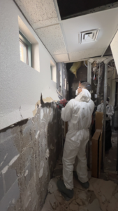 A water damage specialist in a hazmat suit removing damaged wall material during restoration by HTS Restoration in El Paso, TX.