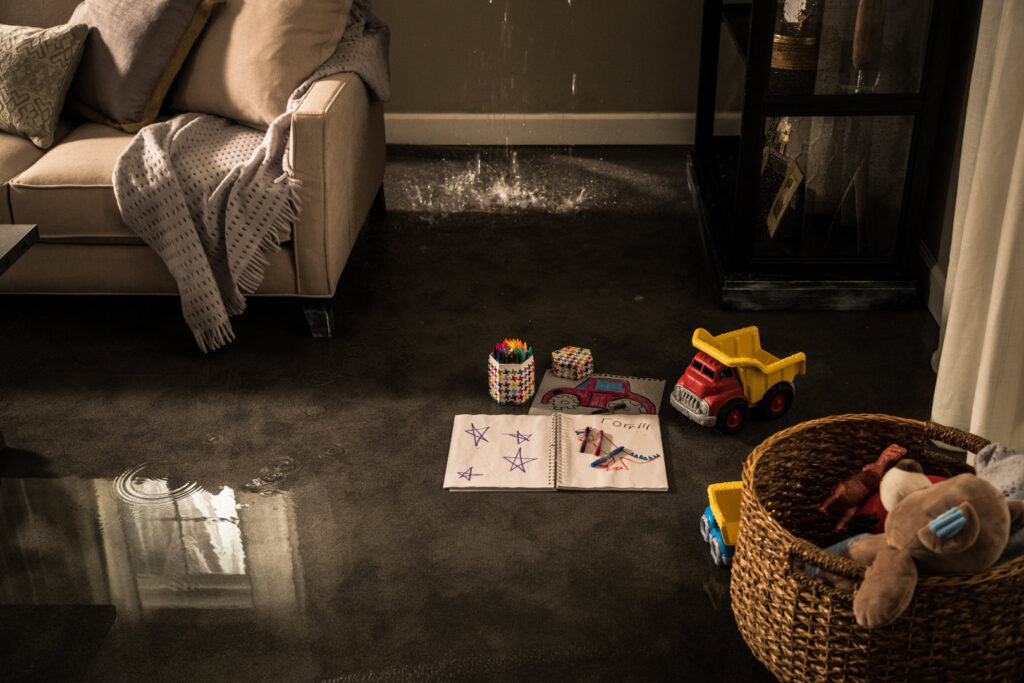 Water actively dripping from a damaged ceiling onto a floor with children's toys, indicating water damage in Lexington, KY.