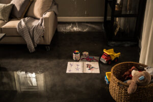 Water actively dripping from a damaged ceiling onto a floor with children's toys, indicating water damage in Lexington, KY.