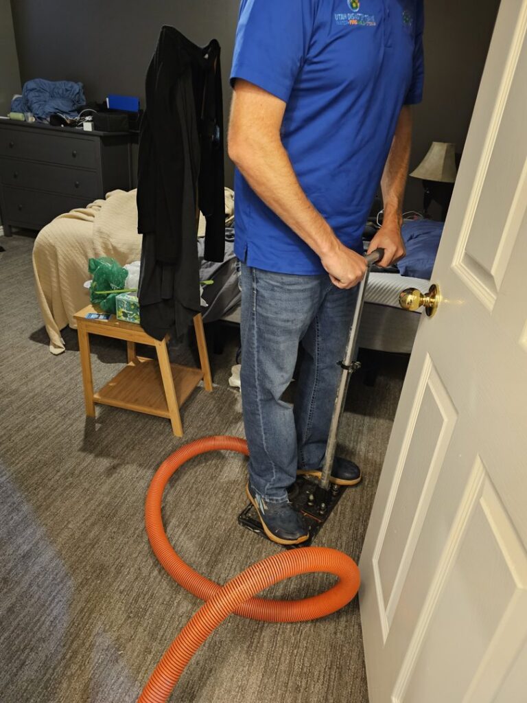 A water damage specialist performs water extraction from a carpeted bedroom floor with professional equipment for Utah Disaster Team in Layton, UT.