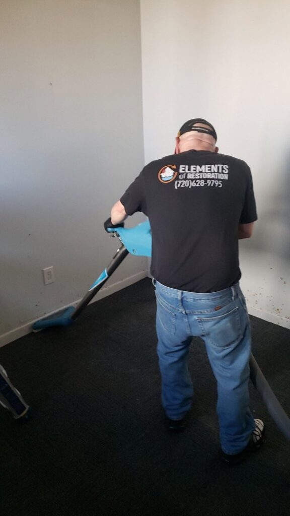 A water damage specialist from Elements of Restoration performing water extraction on a carpeted floor in Denver, CO.