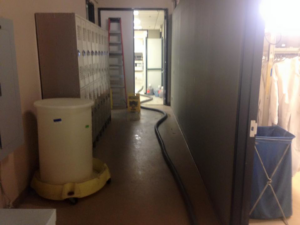 A water extraction hose on a wet floor with a 'wet floor' sign in a commercial hallway by San jose water damage in San Jose, CA