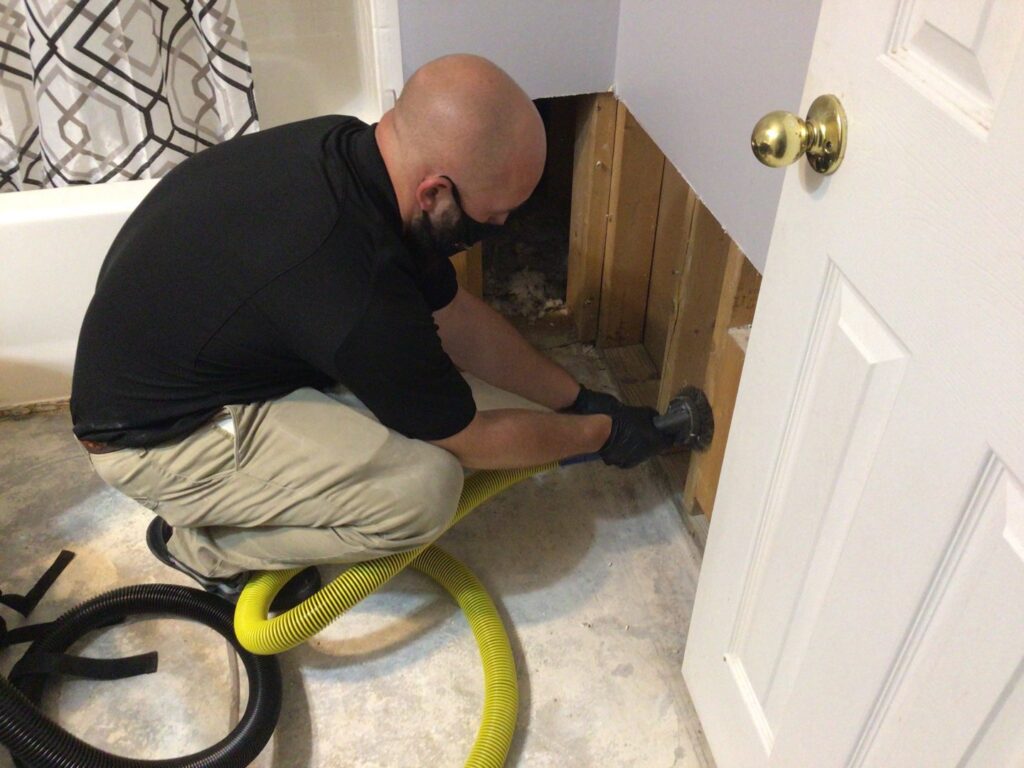 A PuroClean technician performing water extraction from a damaged wall in a bathroom in Northport, AL.