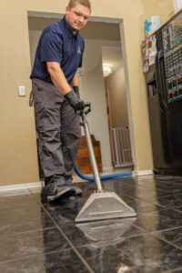 A technician performing water extraction on a wet tiled kitchen floor for TriForce Restoration in Moore, OK.