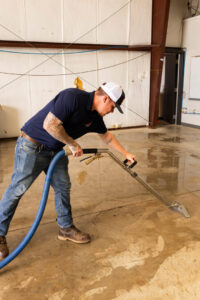 A technician using a water extraction tool on a wet concrete floor for TriForce Restoration in Moore, OK.