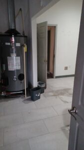 A water heater in a room with a wet and stained floor, indicating water damage, addressed by Elements of Restoration in Denver, CO.