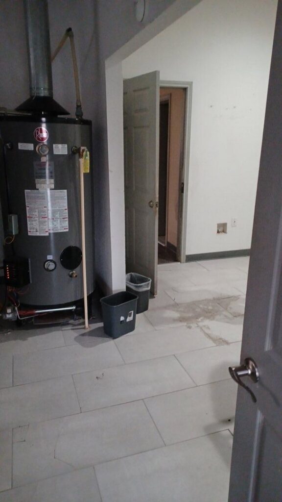 A water heater in a room with a wet and stained floor, indicating water damage, addressed by Elements of Restoration in Denver, CO.