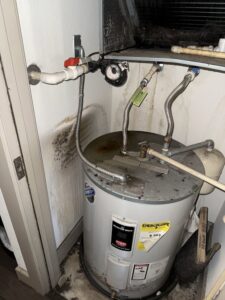 A water heater with significant water stains and mold growth on the wall, indicating a leak addressed by Flow State Restoration in Gilbert, AZ
