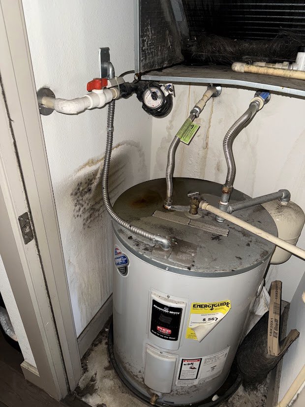 A water heater with significant water stains and mold growth on the wall, indicating a leak addressed by Flow State Restoration in Gilbert, AZ