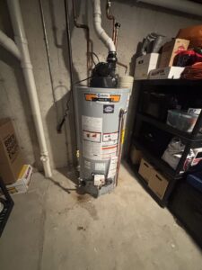 A water heater with a visible puddle and stains on the floor, indicating a leak and water damage, by White Birch Plumbing in Derry, NH.