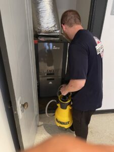 A technician cleans up a water leak near a furnace, a service provided by Directed Heat Restoration in Livonia, MI.