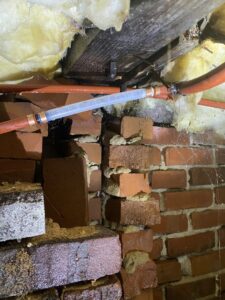 A visible water leak and moisture on a brick foundation and pipes in a crawl space being inspected by Greymen's Plumbing in Rock Hill, SC.