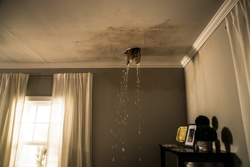 Water pouring from a hole in a ceiling with visible water stains, showing severe water damage in Lexington, KY.