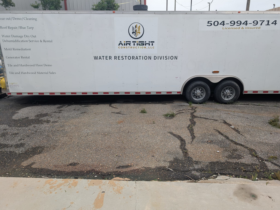 A white trailer for Air Tight Construction's Water Restoration Division, listing services like water damage dry out and mold remediation in Kenner, LA.